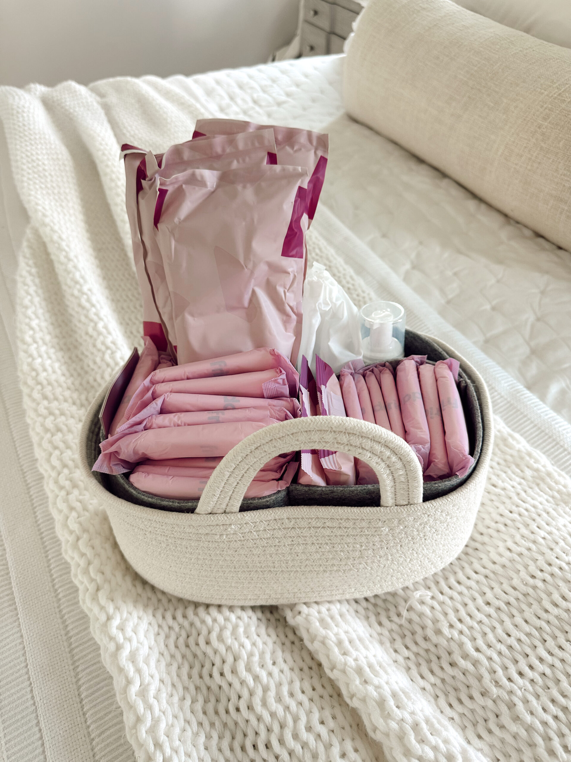 Postpartum basket filled with pads, recovery items, and toiletries on a white blanket
