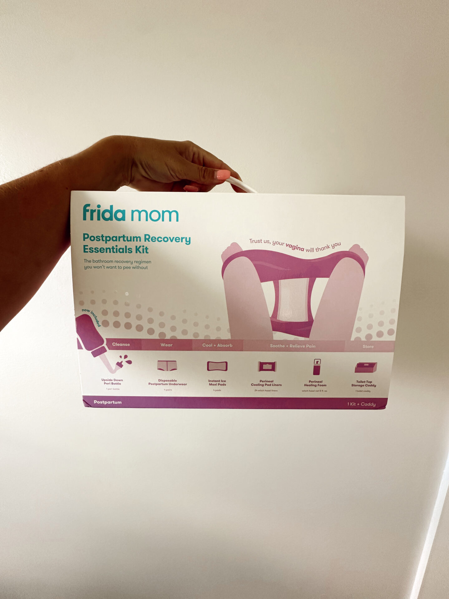 Frida Mom Postpartum Recovery Essentials Kit held in hand against a white wall