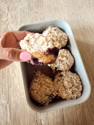 Close-up of a sourdough discard blueberry muffin with crumb topping, held in hand.